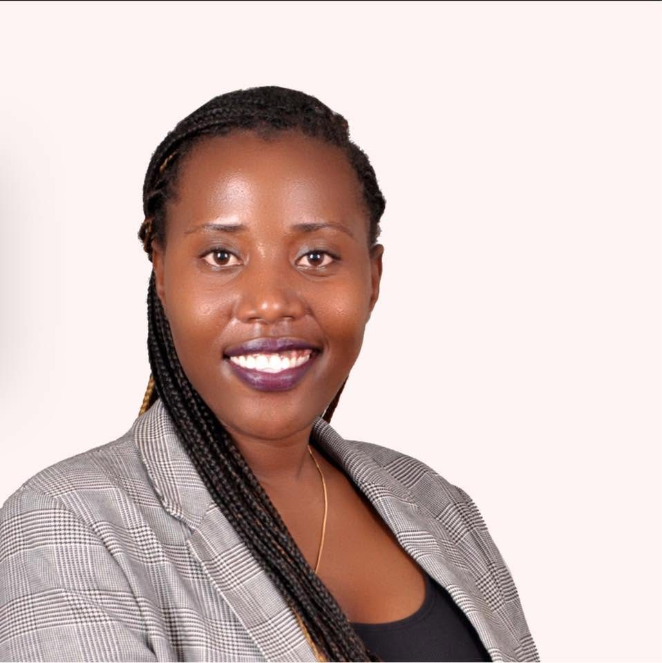 Portrait of SHELIFT founder Dorah Nakagga smiling, wearing a grey checked blazer