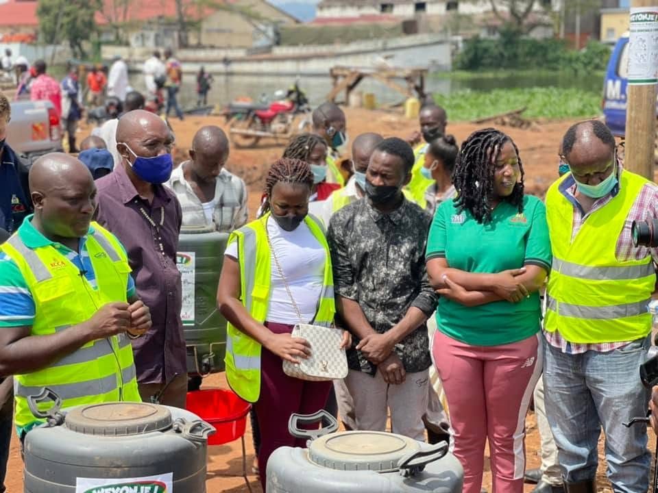 Community members in high-visibility vests stand behind water containers at an outdoor distribution