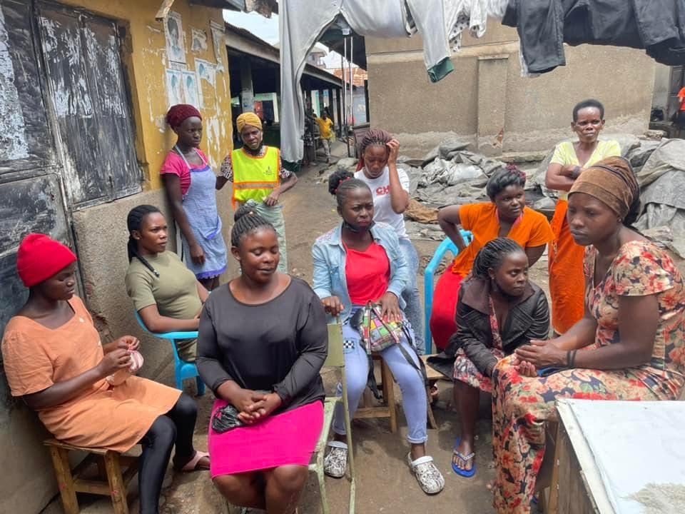 Women and girls sit together on benches in a community courtyard during a group session