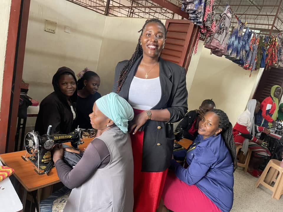 A smiling woman stands among women working at sewing machines in a tailoring workshop