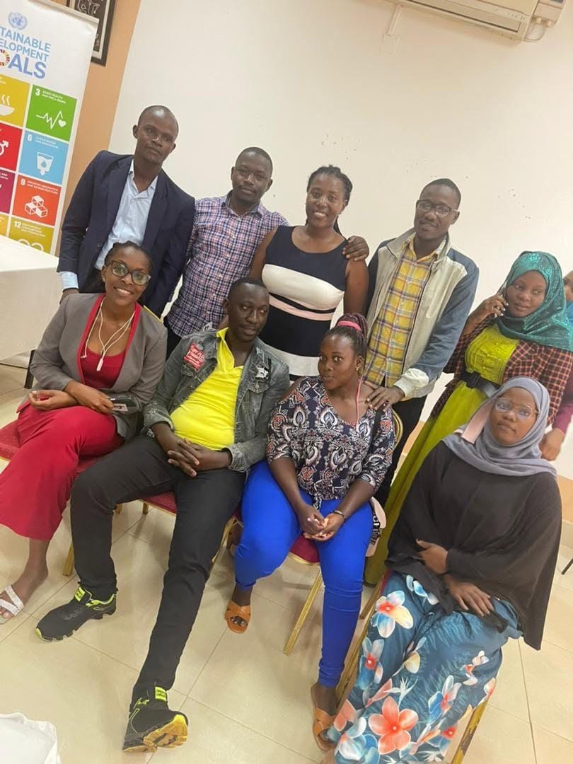 A group of young women and men pose together beside a Sustainable Development Goals banner