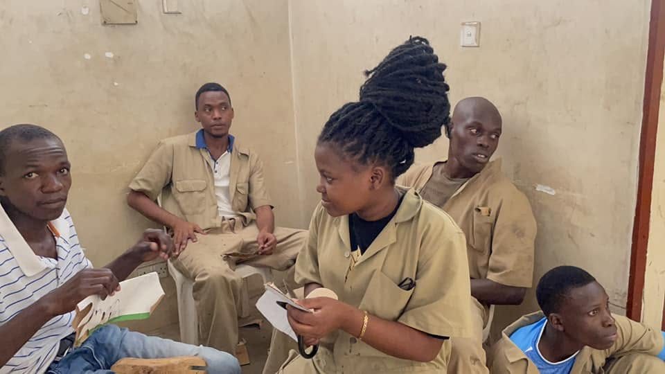 A young woman in a khaki workshop uniform holds notes during a vocational training session