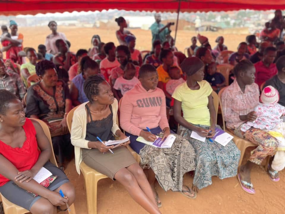 Women and girls sit under a tent taking notes during a community training session
